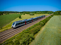 Ein silber-roter Zug des Typs Bombardier Talent 2 von DB Regio fährt durch eine Frühlingslandschaft