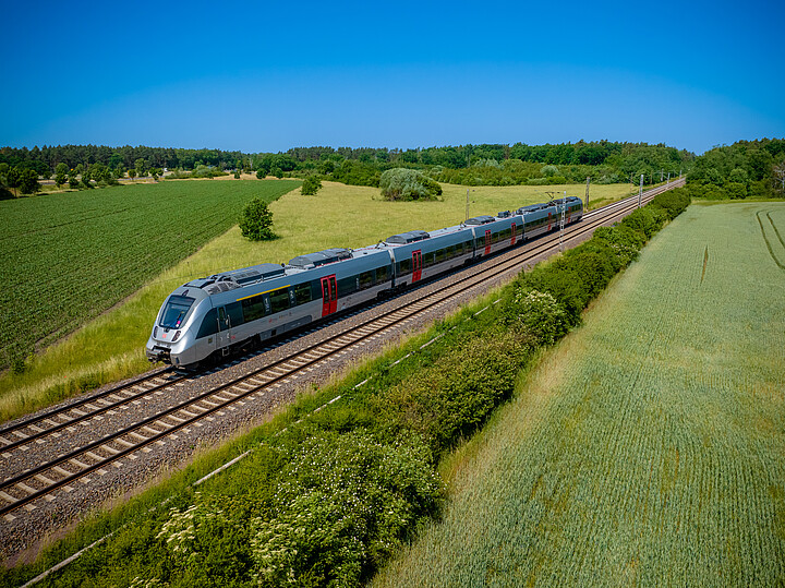 Ein silber-roter Zug des Typs Bombardier Talent 2 von DB Regio fährt durch eine Frühlingslandschaft
