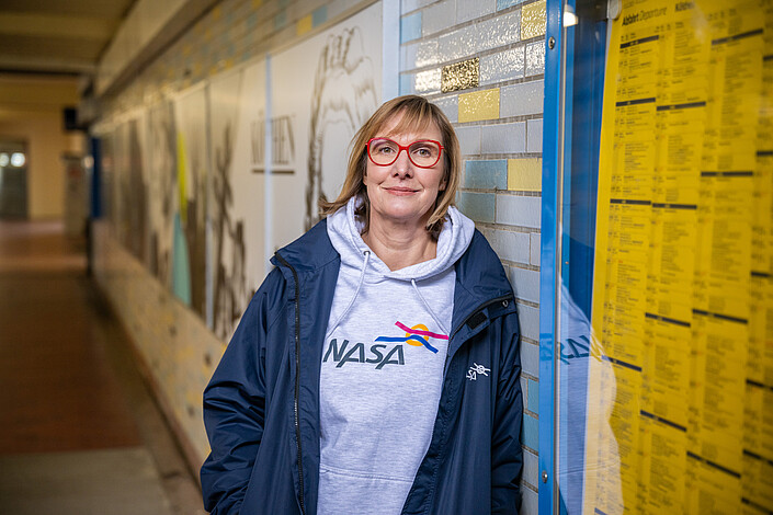 Eine Frau (Doreen Havemann) steht in einer Bahnunterführung. Sie trägt eine Jacke und einen Pullover, die mit dem Logo der NASA GmbH bedruckt sind