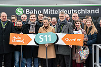Verkehrsministerin Lydia Hüskens steht mit Gästen und Politikern vor einem neu gestalteten Zug der S11. Sie hält ein Schild mit dem türkisfarbenen S11-Logo in der Hand, daneben die Ziele Halle (Saale) und Querfurt. Auf dem schwarz-grün-grau gestalteten Zug steht "S-Bahn Mitteldeutschland".