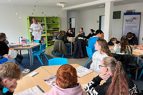Eoine Unterrichtssituation in einem Klassenraum. In der Mitte steht Frau Havemann