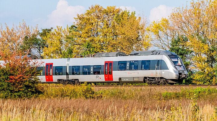 Ein silber-roter Zug des Typs Bombardier Talent 2 von DB Regio fährt durch eine herbstliche Landschaft