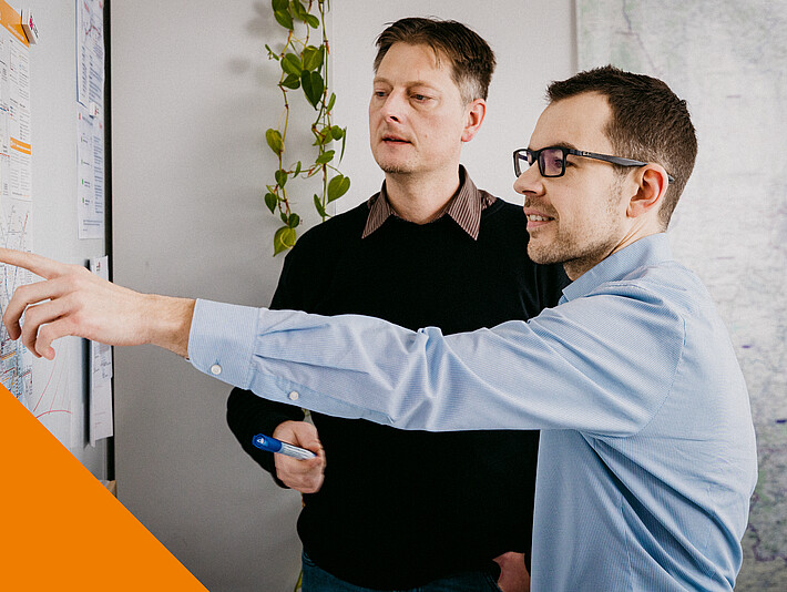 Zwei Männer schauen sich an einer Wand hängende Liniennetzpläne an