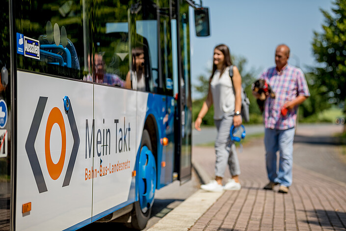 Eine Frau und ein Mann steigen in einen Bus, auf dem das Mein-Takt-Logo zu sehen ist
